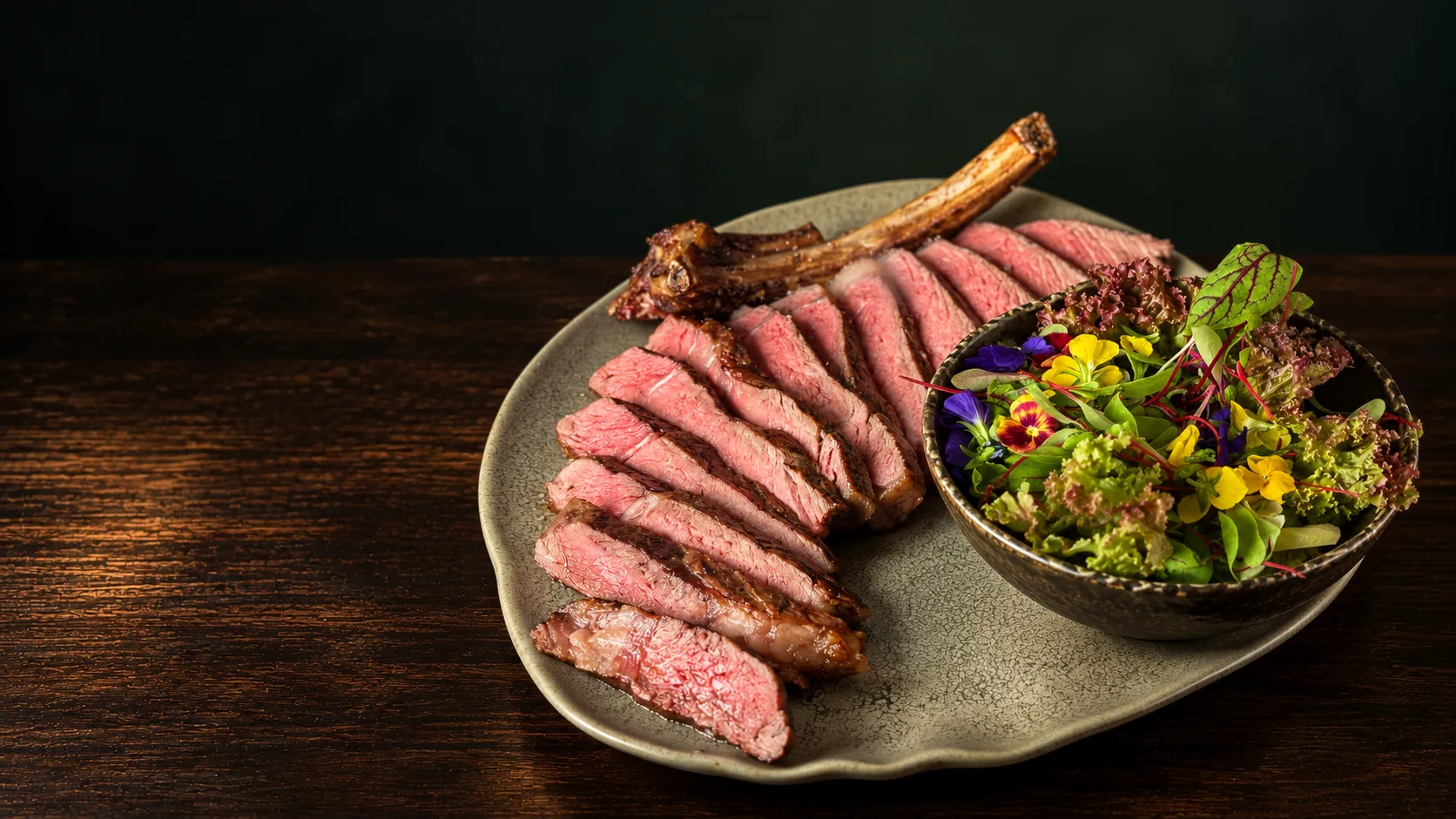 Sliced bone-in steak with a salad of leaves and edible flowers